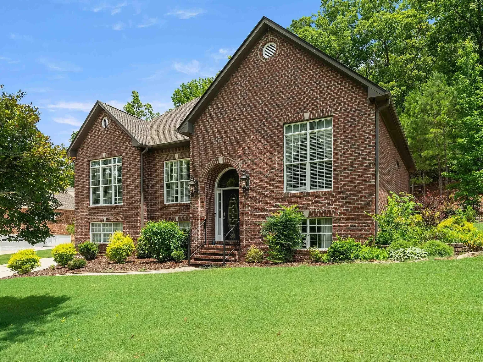 Front view of a two-story brick house with large windows, a black front door, and a landscaped lawn with bushes and trees.