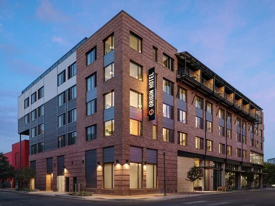 A modern multi-story hotel building with a brick facade and large windows at dusk