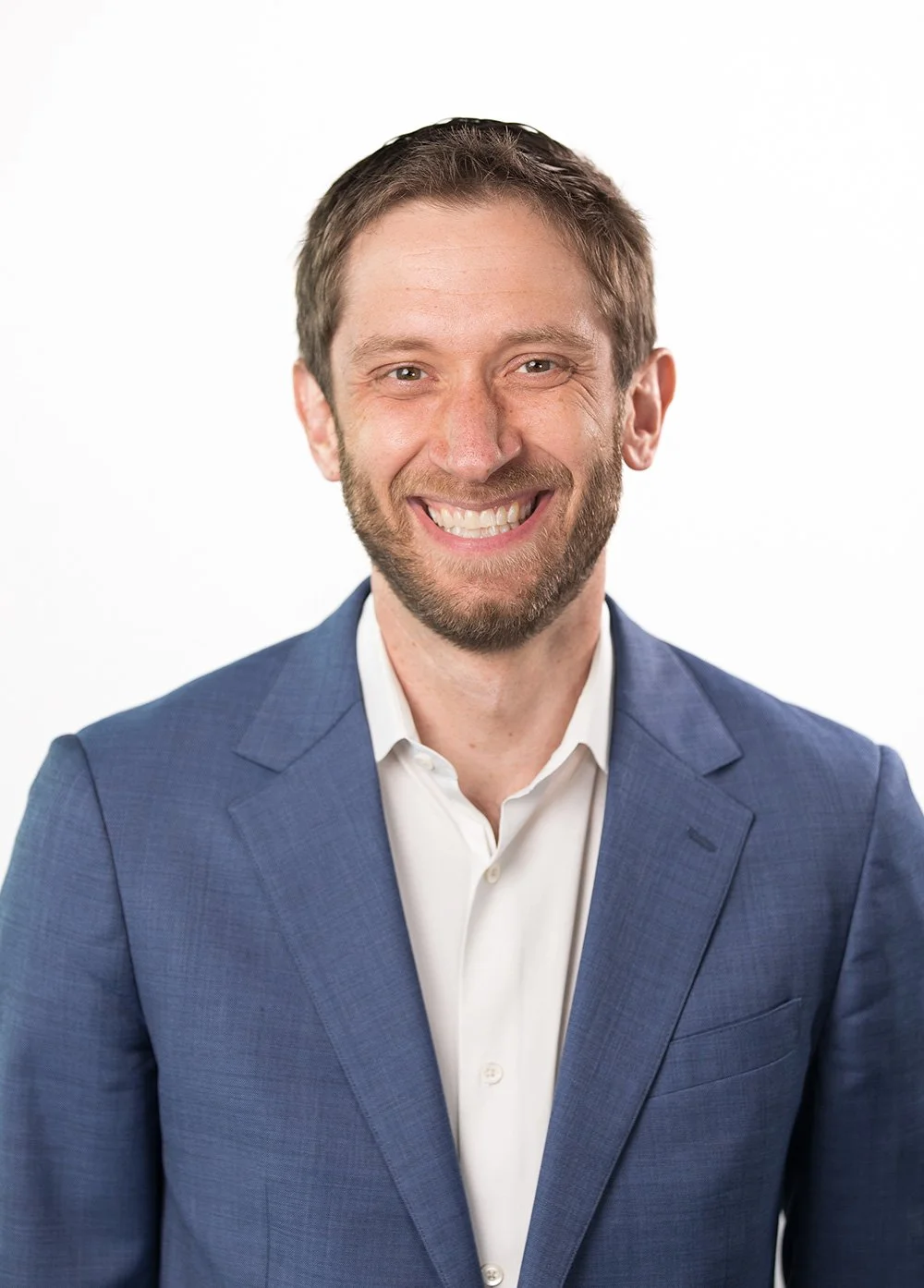 Portrait of a smiling man in a blue suit and white shirt on a white background.