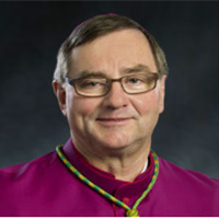 Portrait of a man wearing glasses and a purple shirt with a necklace, smiling at the camera.
