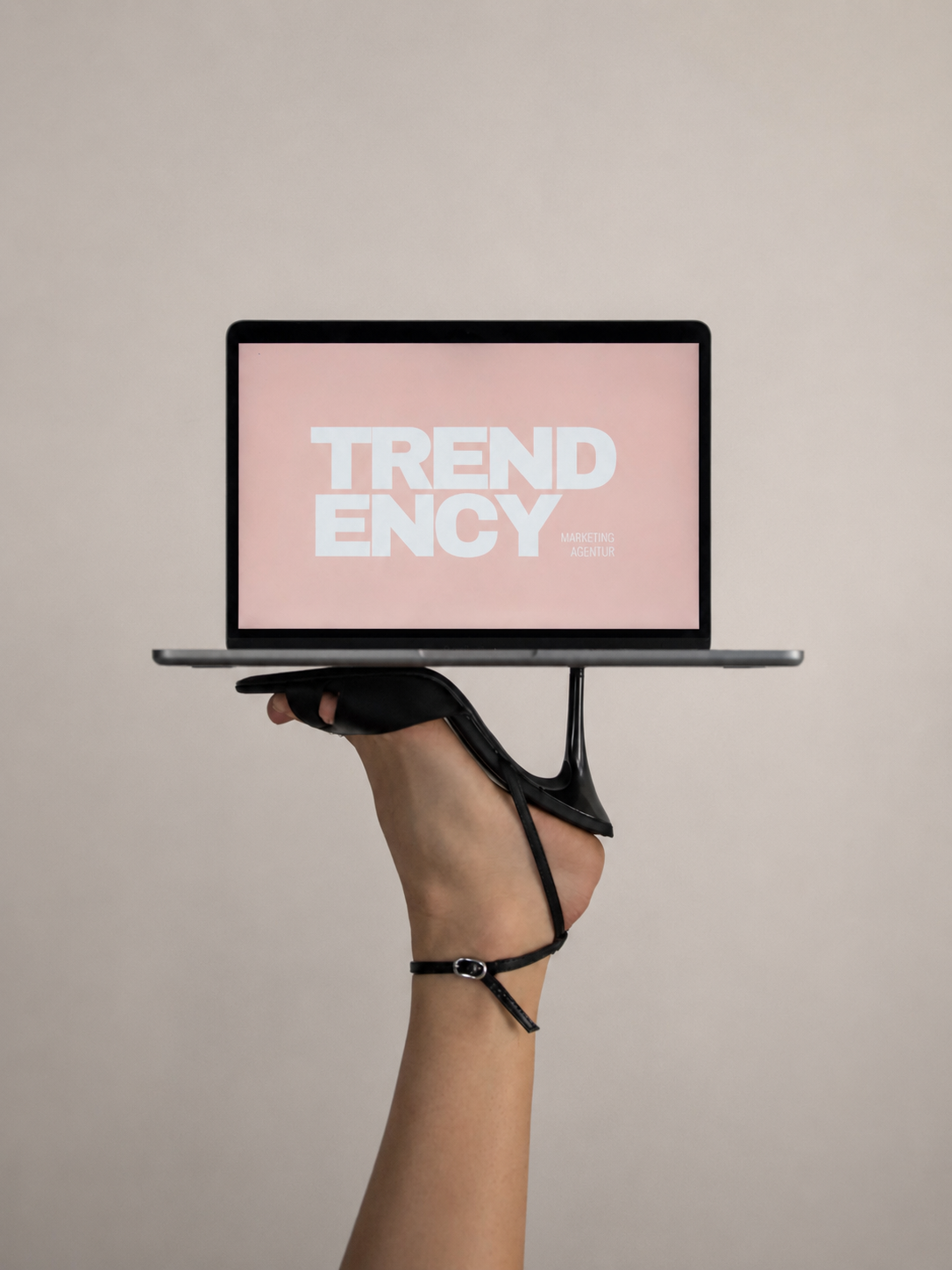 Hand hält einen Laptop mit einem Bildschirm, der den Text "TREND ENCY" anzeigt, auf einem einfachen, hellen Hintergrund.
