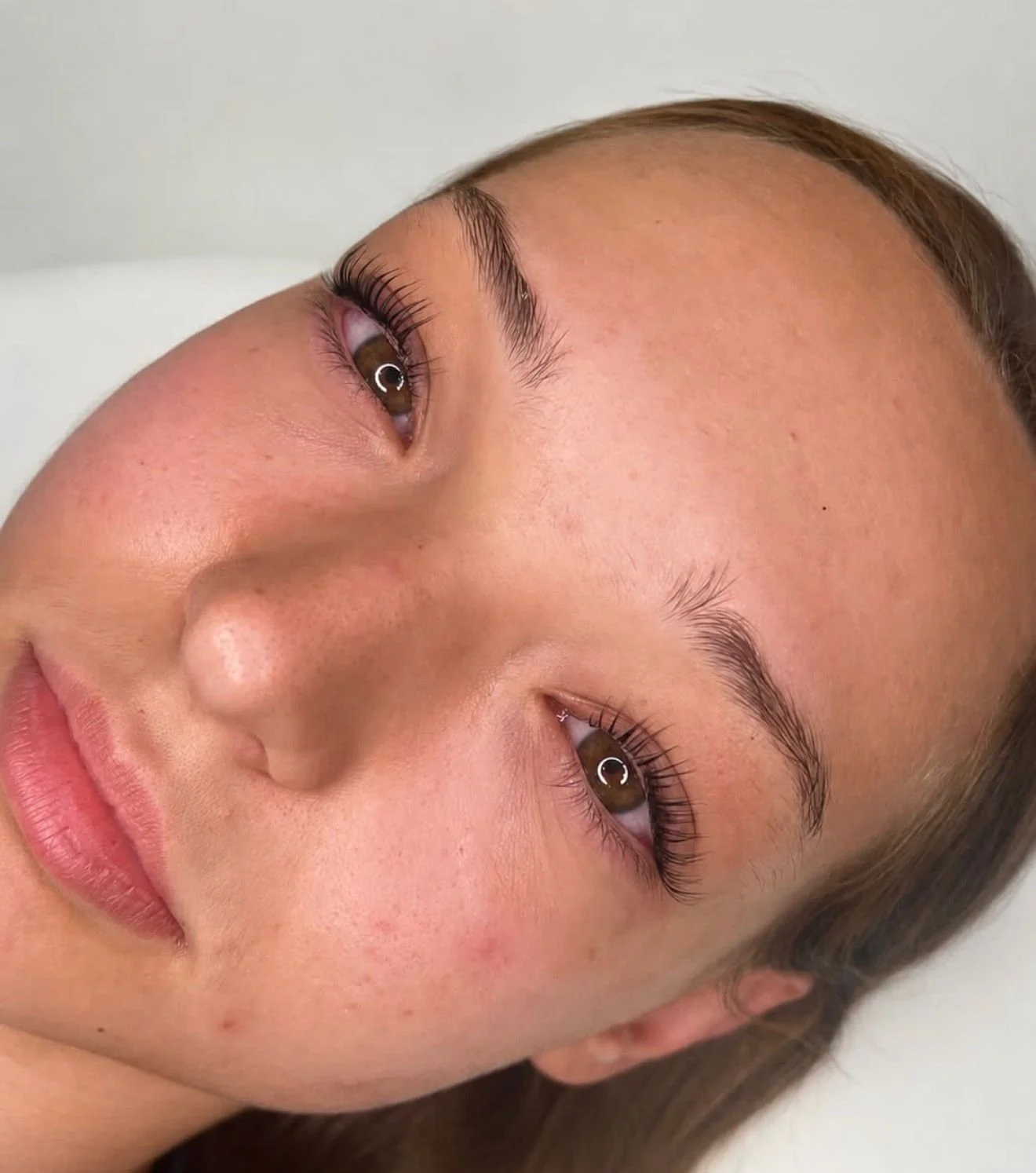 Close-up of a woman's face showing her brown eyes, well-groomed eyebrows, and smooth skin with some natural freckles.
