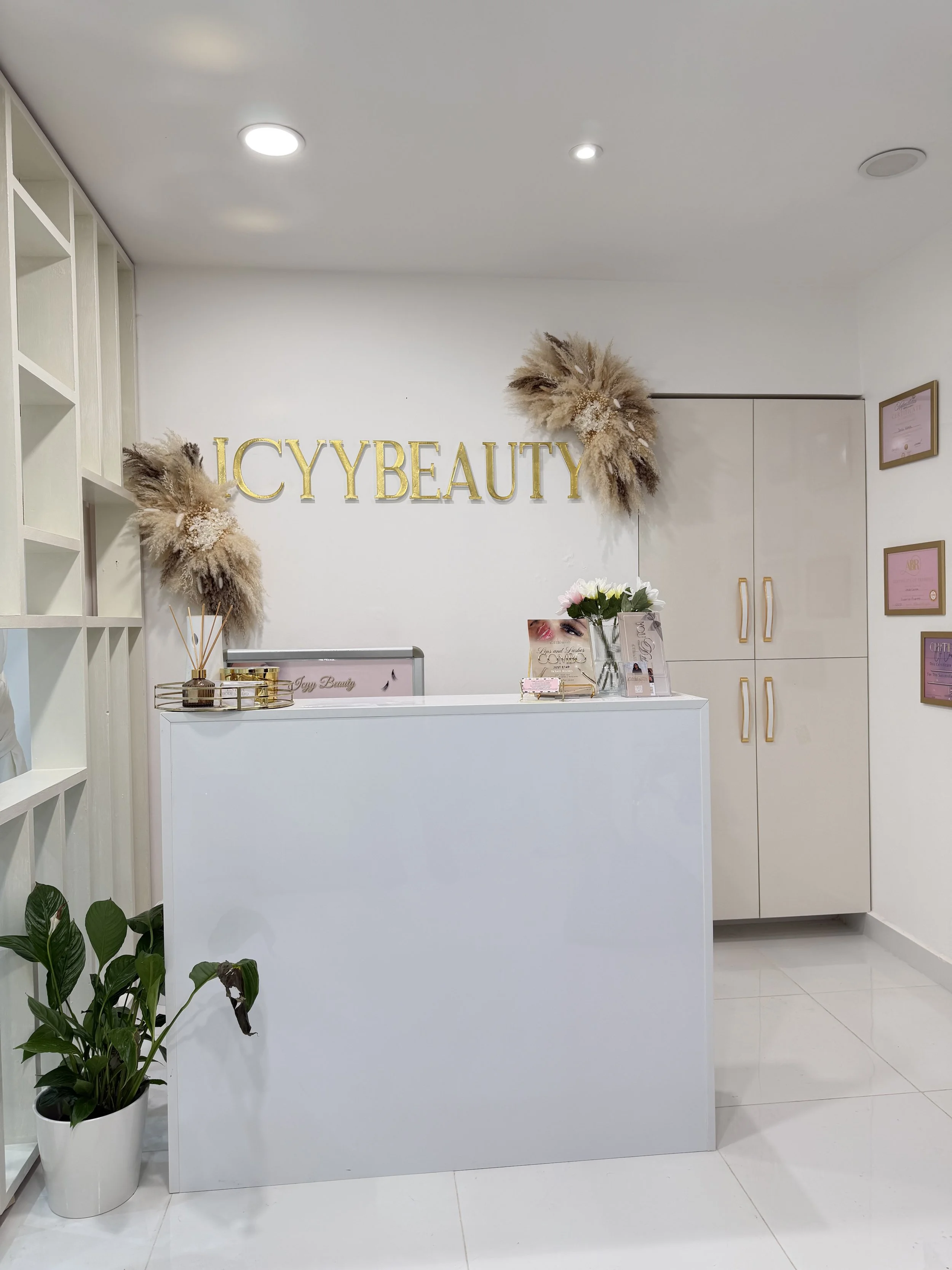 Reception desk at ICCY Beauty with a white counter, decorative flower arrangements, and gold signage on the wall.