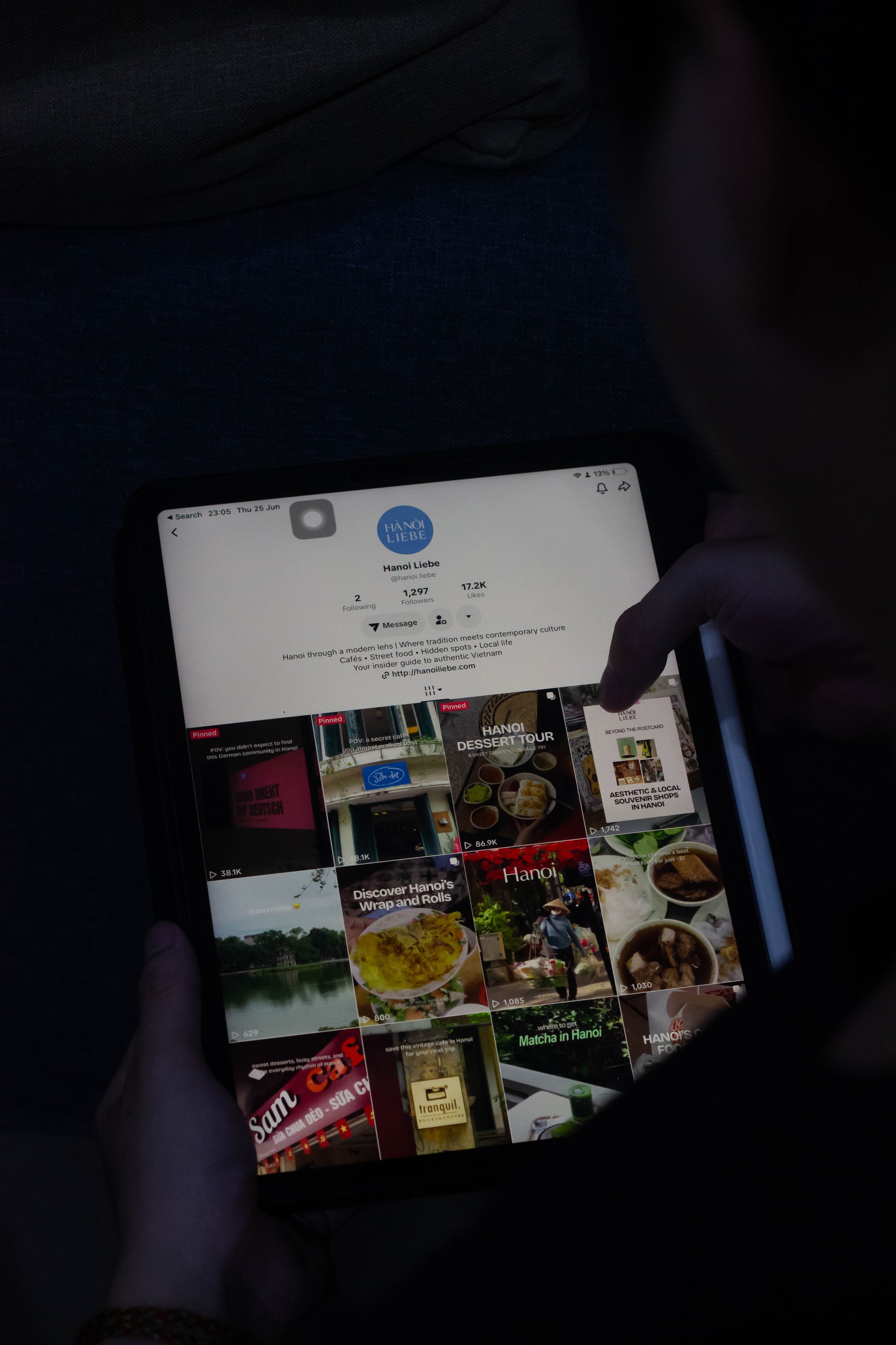 A person holding a smartphone displaying a social media profile for 'Hanoi Liebe,' a travel and culture guide for Hanoi, Vietnam, with various video thumbnails related to destinations and food in Hanoi.