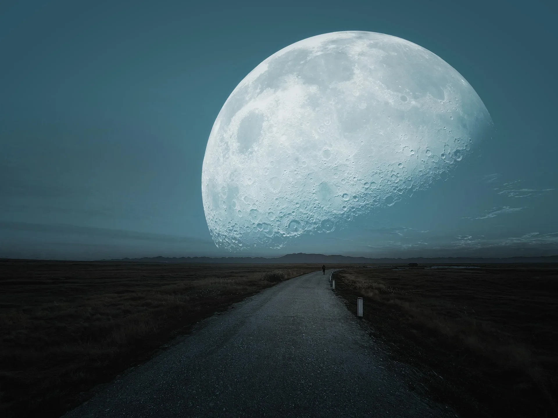 A person walking on a dirt road in a vast landscape with mountains in the distance, under a large, bright full moon in the night sky.