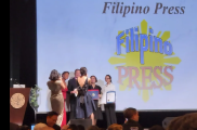 People on stage at a Filipino Press event with a large screen displaying the event name in Filipino and English.