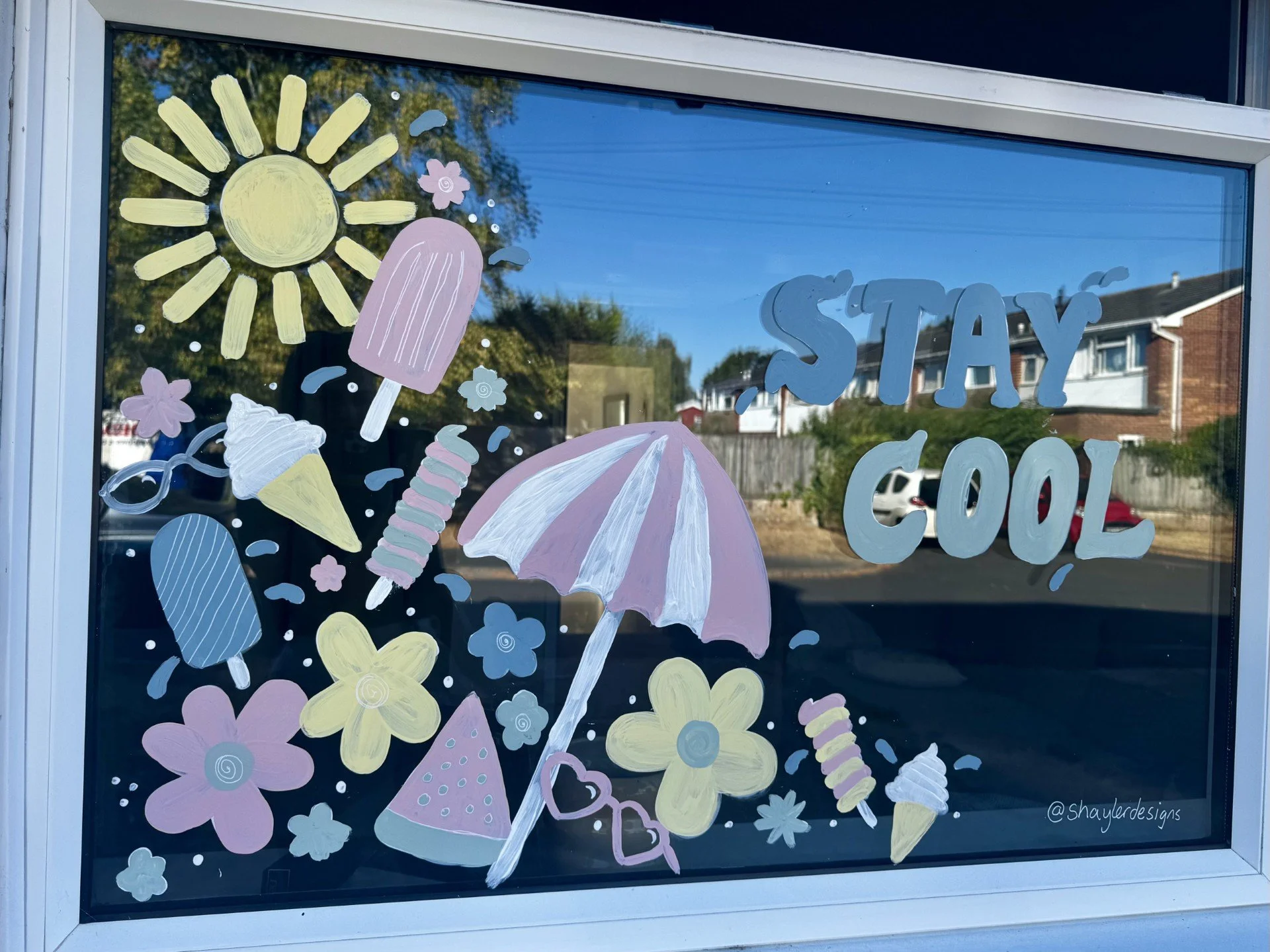 Decorative window with pastel-colored drawings of suns, umbrellas, flowers, ice cream cones, popsicles, hearts, and the words "STAY COOL" in light blue lettering.