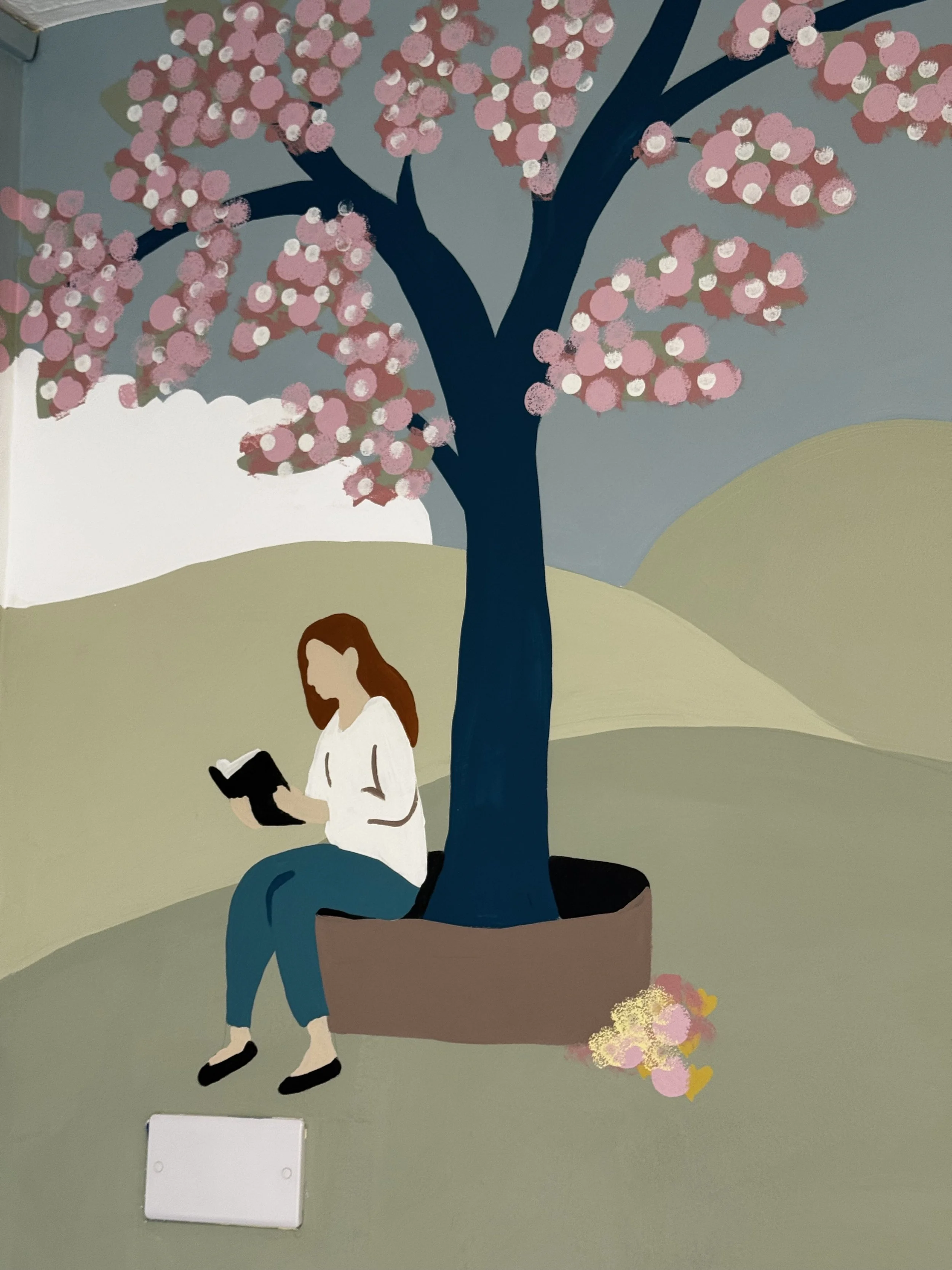 A mural of a person with long hair reading a book, sitting under a tree with pink blossoms, on a light green background.