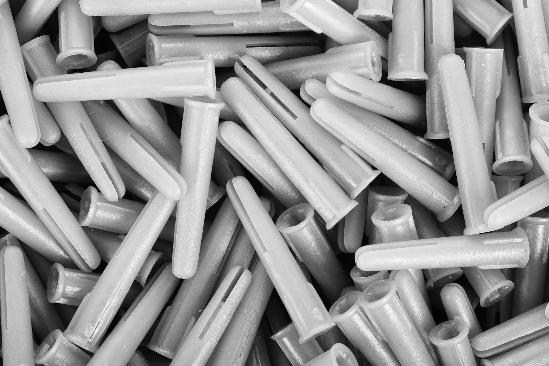 A black-and-white photo of numerous plastic wall anchors, also called expansion anchors, used for anchoring screws into drywall or other materials.