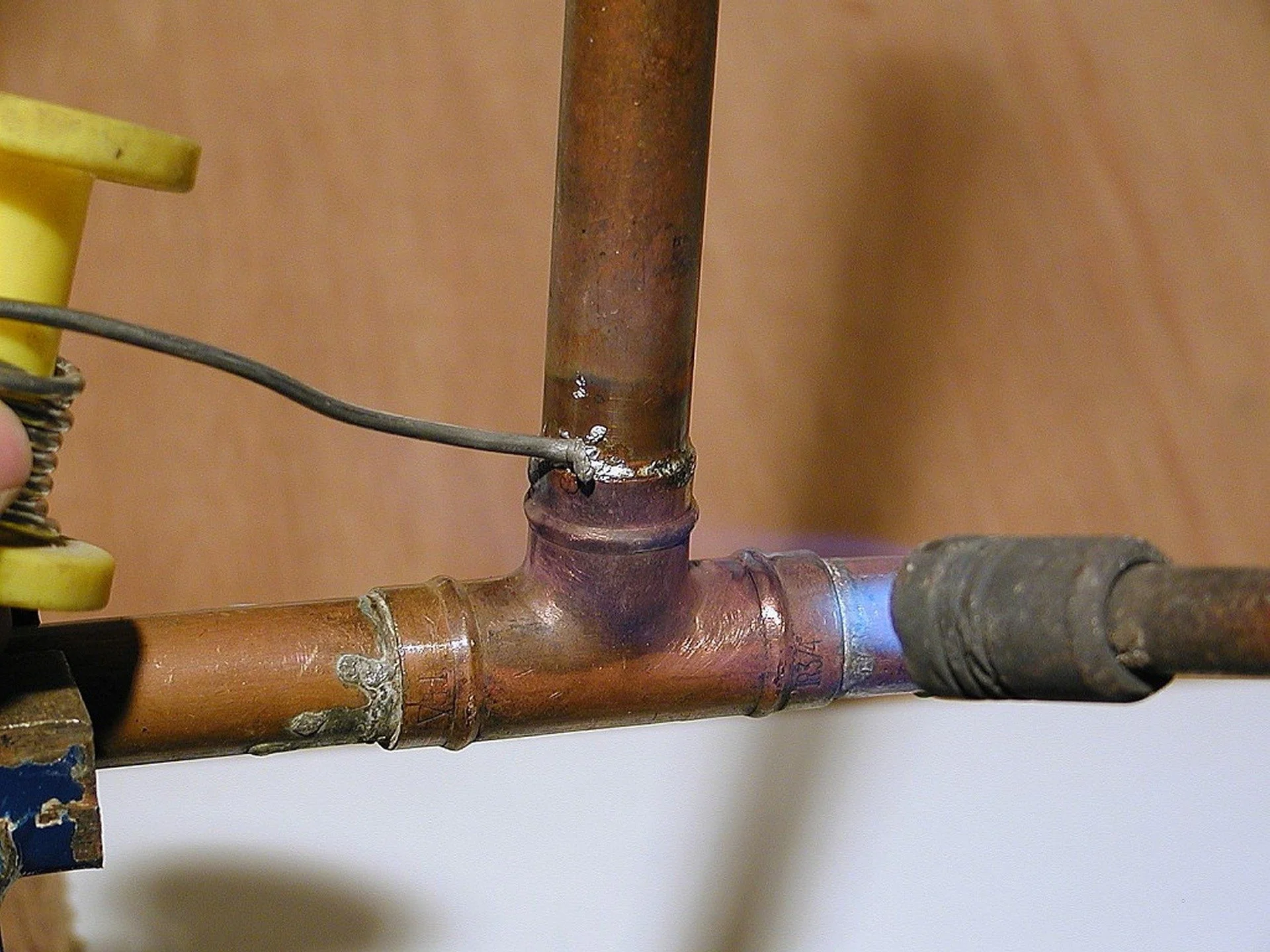 Close-up of rusty copper plumbing pipes with a yellow valve and a connected metal wire.