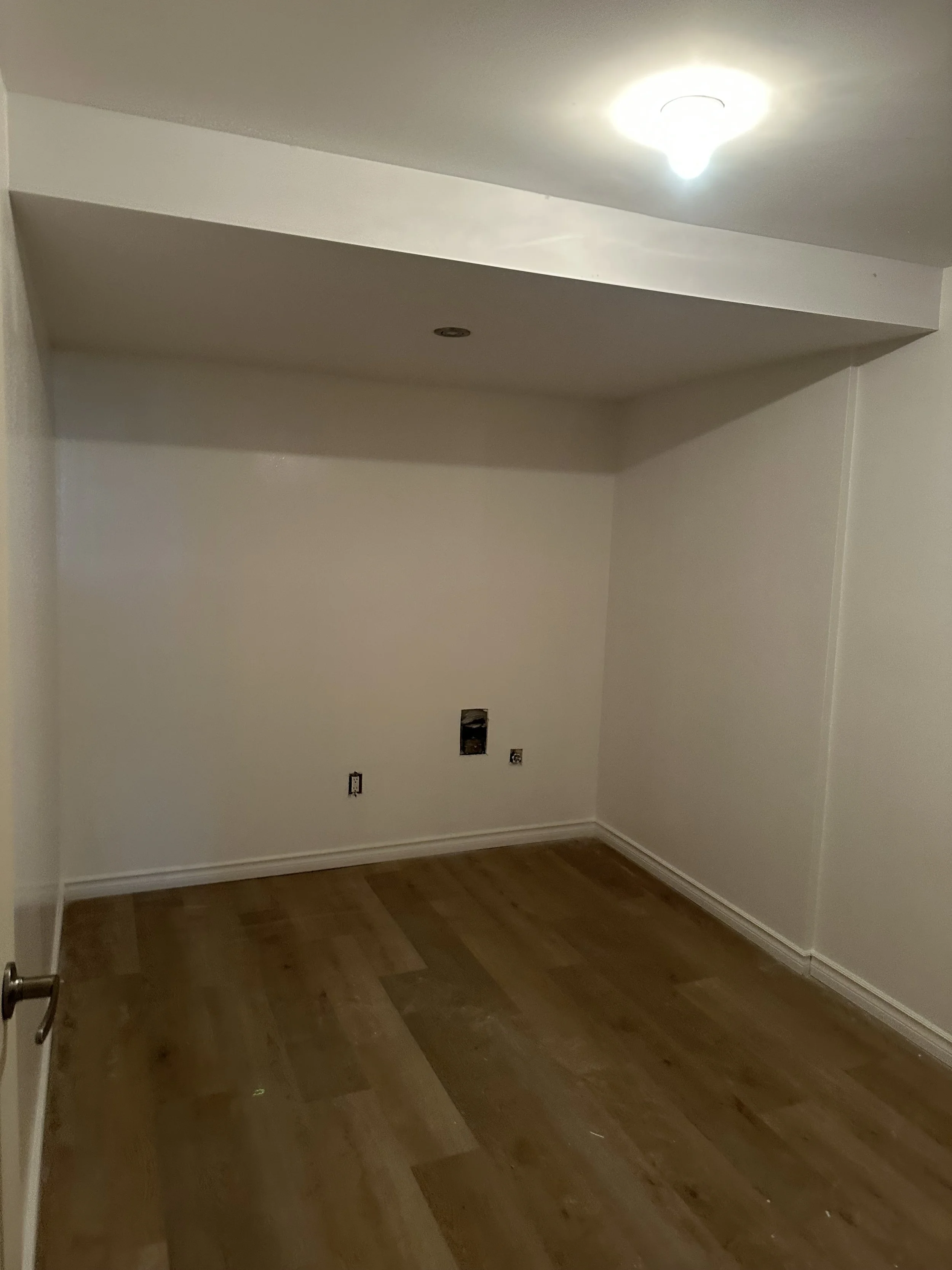 Empty room with wood flooring, white walls, no furniture, ceiling light, electrical outlets, and an unfinished wall inlet.