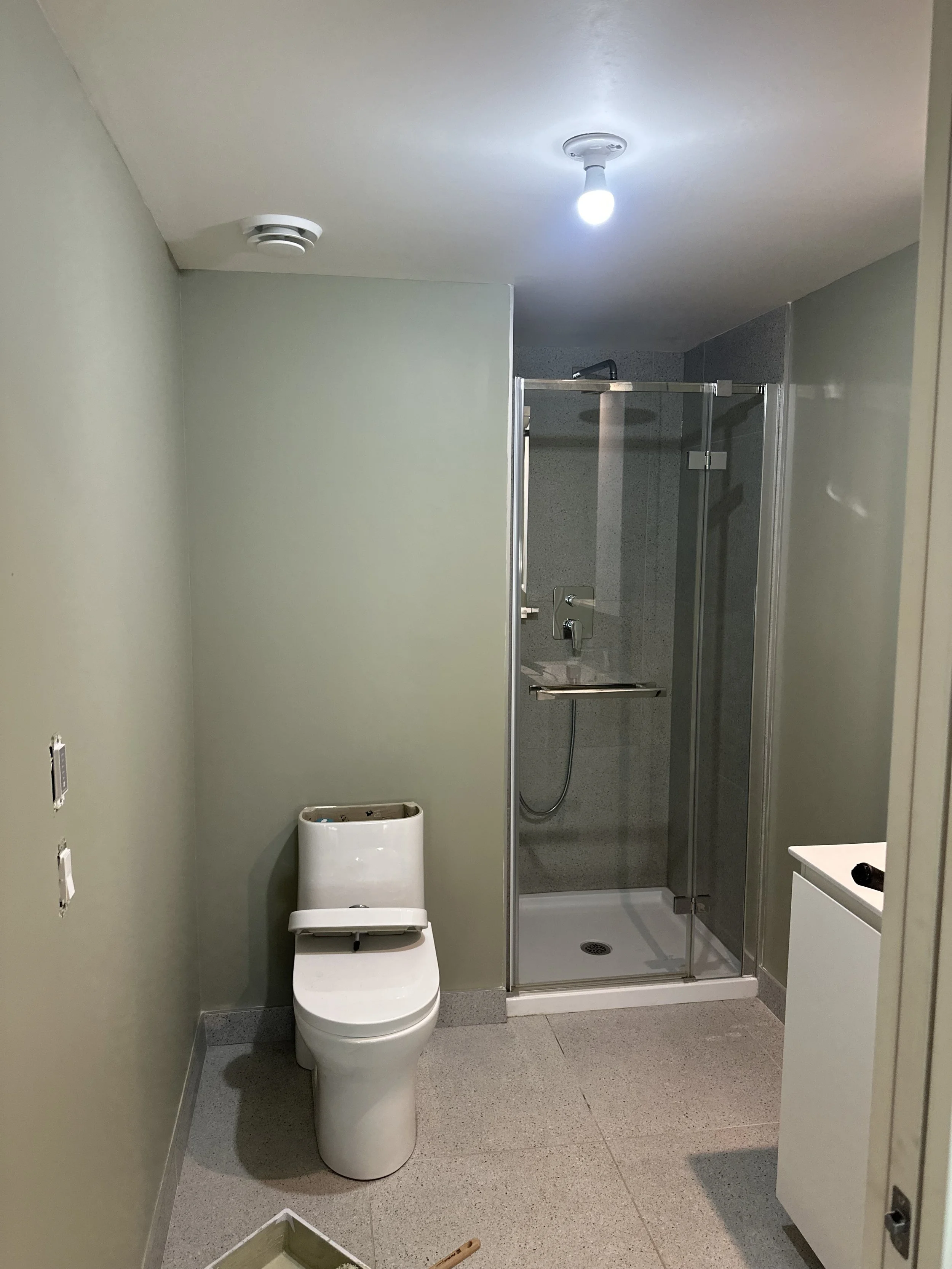 A bathroom with a modern toilet, a shower enclosure, and a small white cabinet. The bathroom appears to be under renovation or construction.