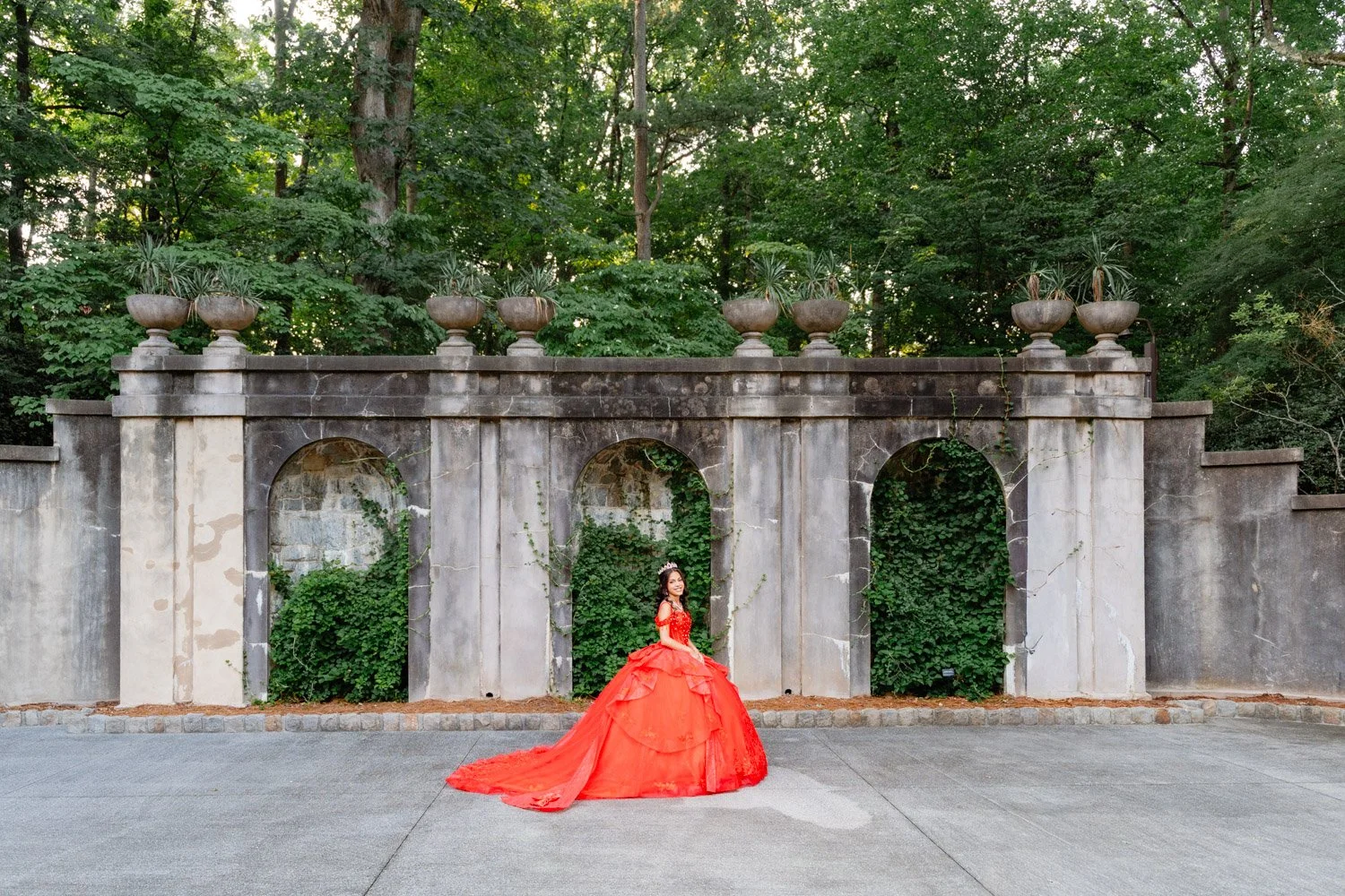 Quinceañera con vestido rojo frente a los arcos de un jardín