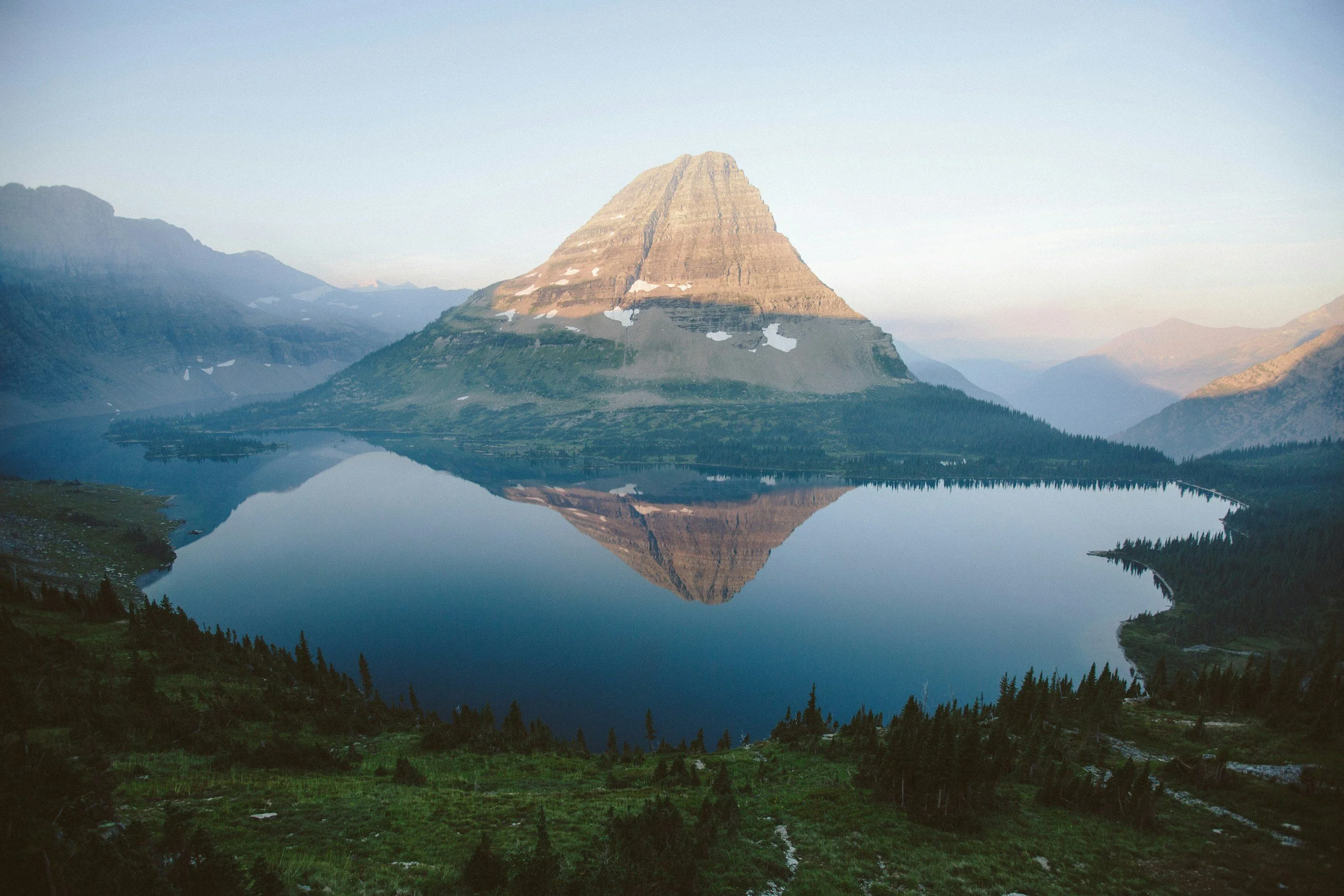 A mountain with a conical shape reflected in a calm lake with forested shores.