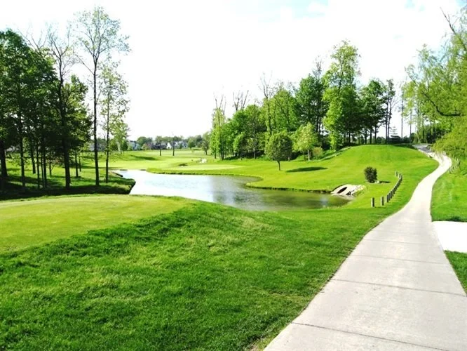 A golf course with a paved walking path, a small pond, and green trees in springtime.