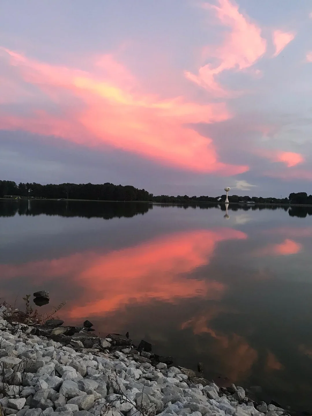 Pink and purple clouds reflected on a calm body of water near a rocky shoreline