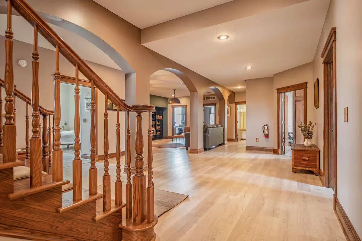 Spacious entryway with hardwood floors, wooden staircase, and multiple archways leading to other rooms, with furniture and decor visible in the background.