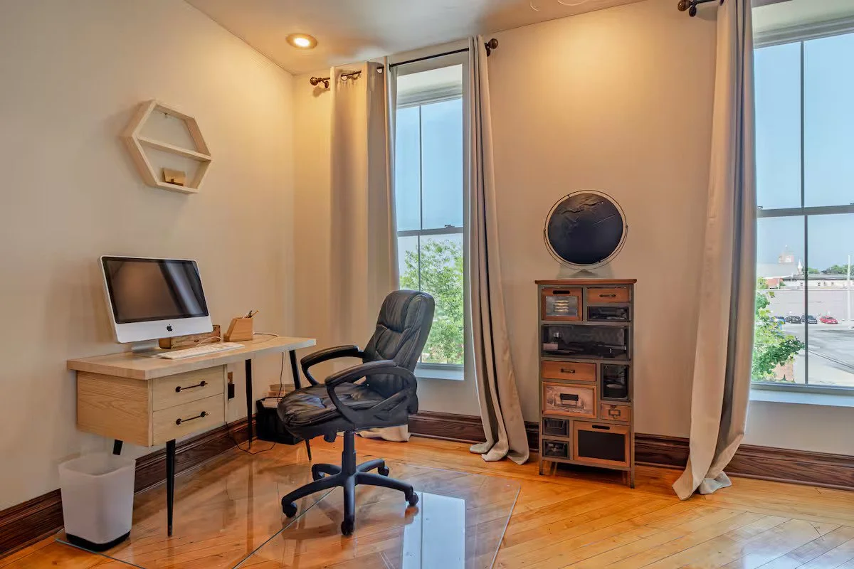 Home office with a desk, computer, office chair, wooden cabinet, and large windows with curtains.