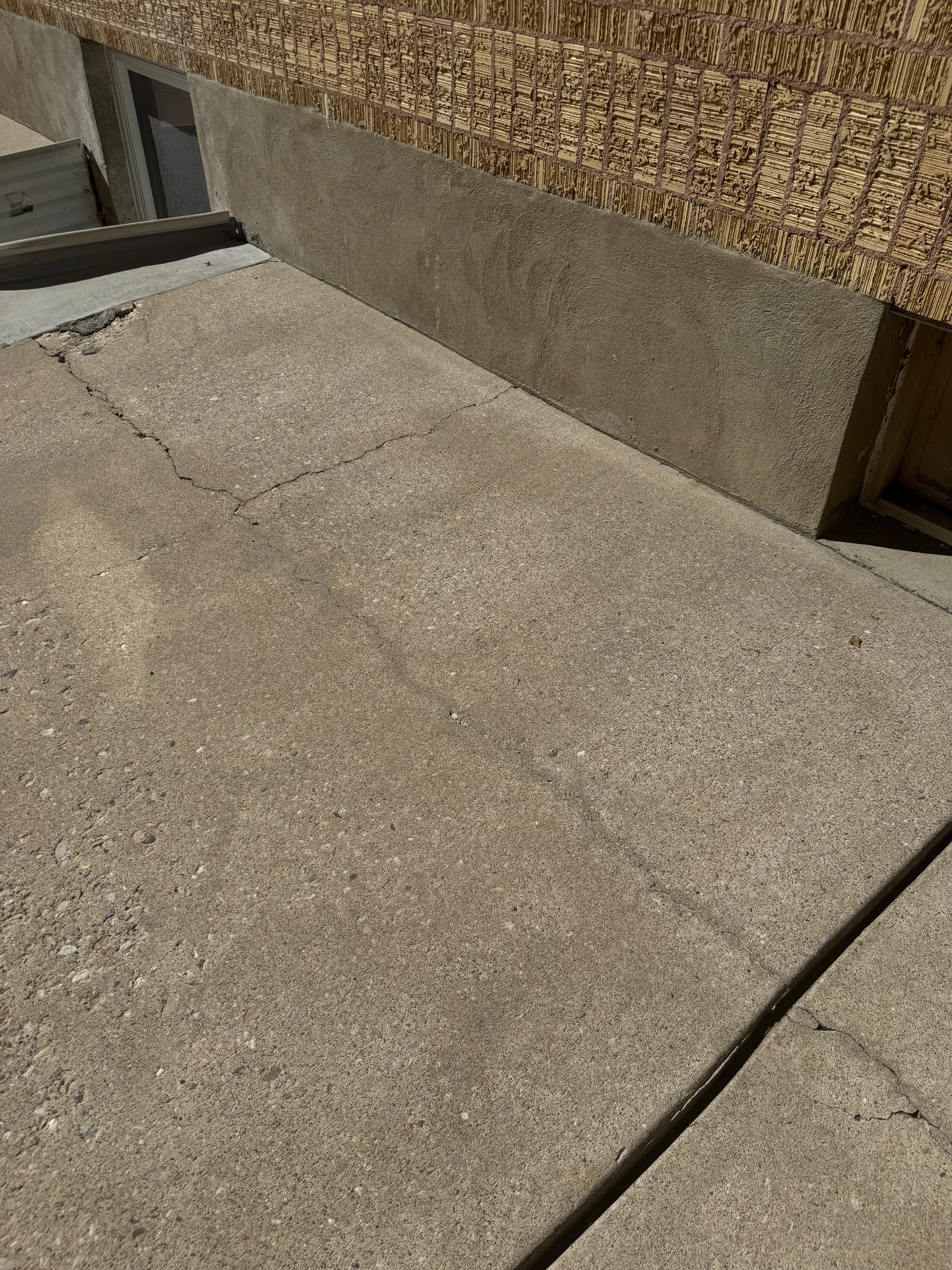 Concrete porch with cracks, view of a window, wall with brick and stucco, and some black wire in the corner.