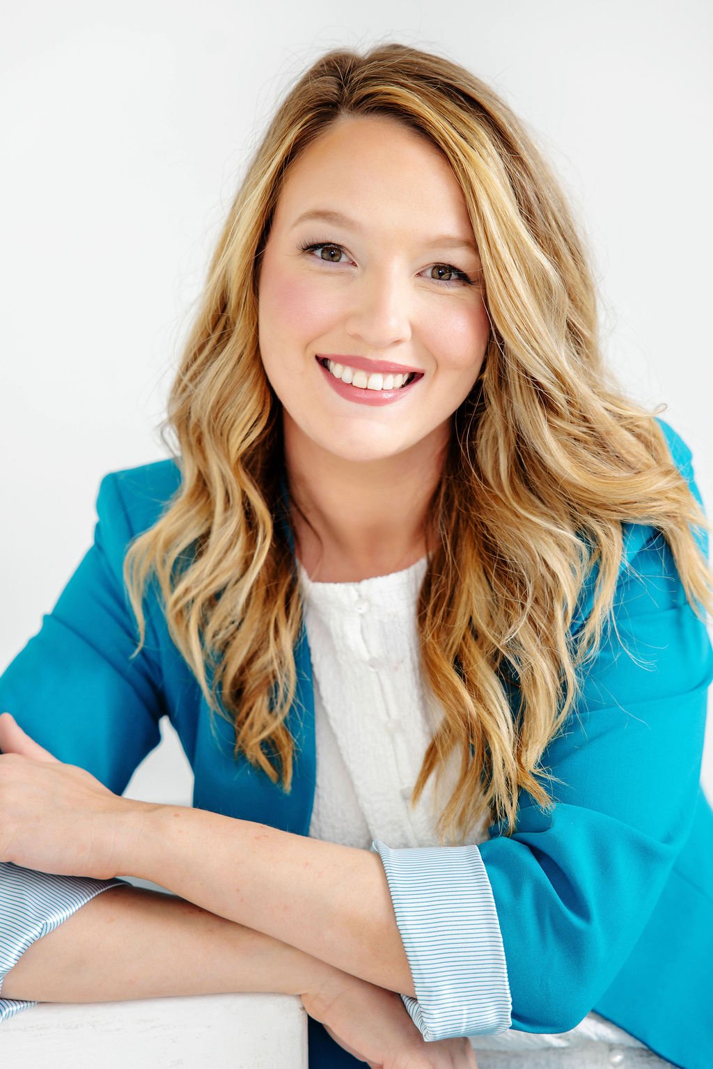 Headshot of Taylor Dreigon smiling with long wavy blonde hair wearing a bright blue blazer and white top against a plain white background.