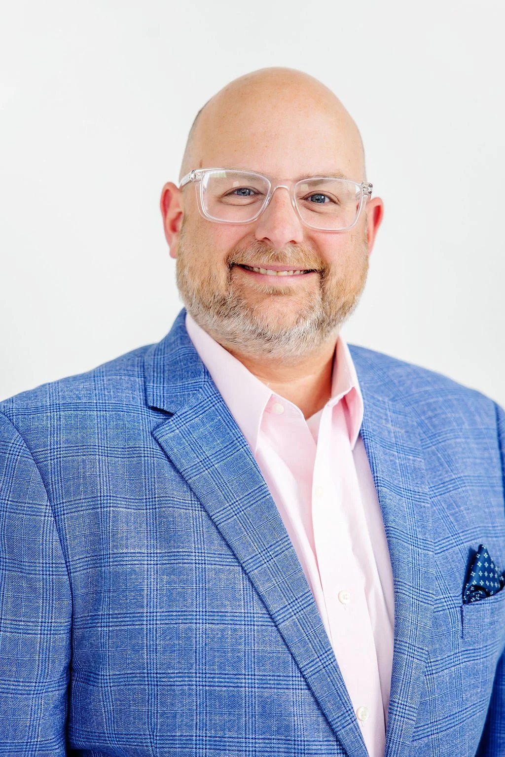 Brian Jones, paralegal, smiling with glasses, wearing a pink shirt, a blue checkered blazer, and a pocket square, standing against a white background.