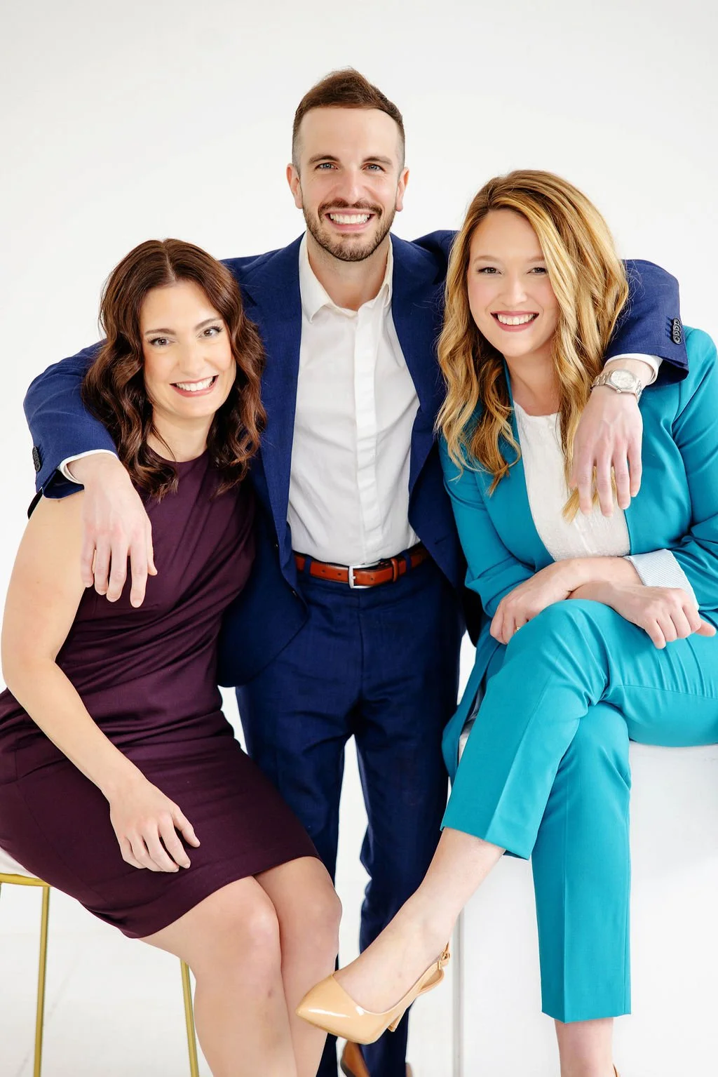 Alison DeVilliers, Austin Li Puma, and Taylor Dreigon dressed in business attire, posing together with Austin in the center and the women sitting on chairs. All have their arms around each other.
