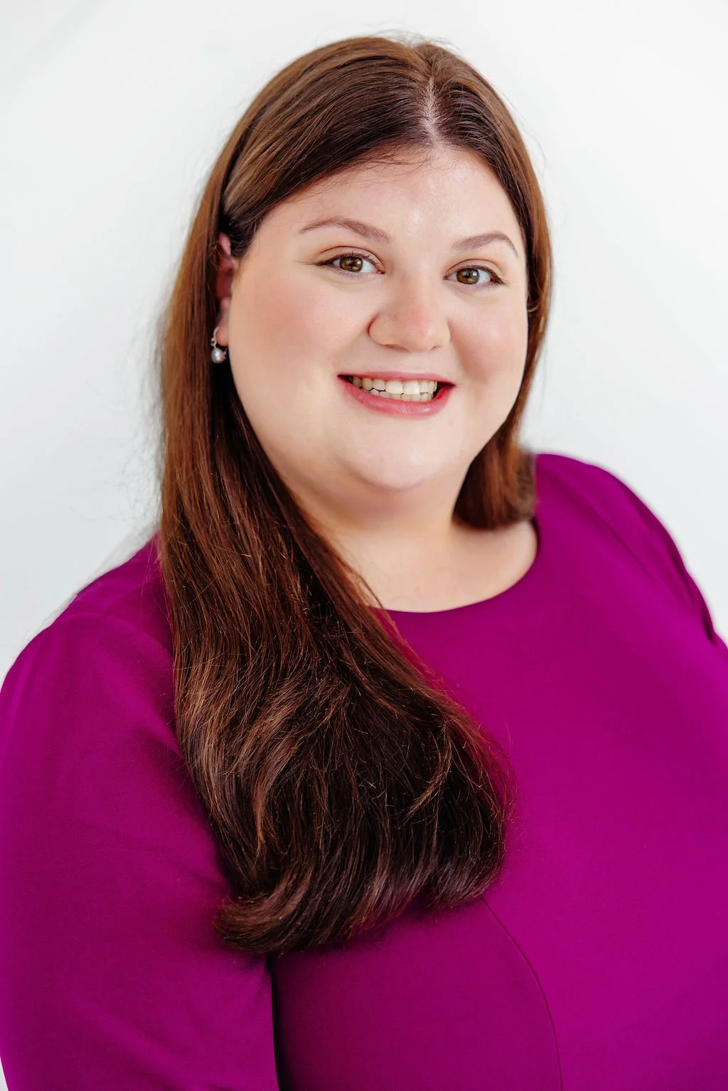 Jami Diamond smiling, wearing a purple top and pearl earrings, smiling against a plain white background.