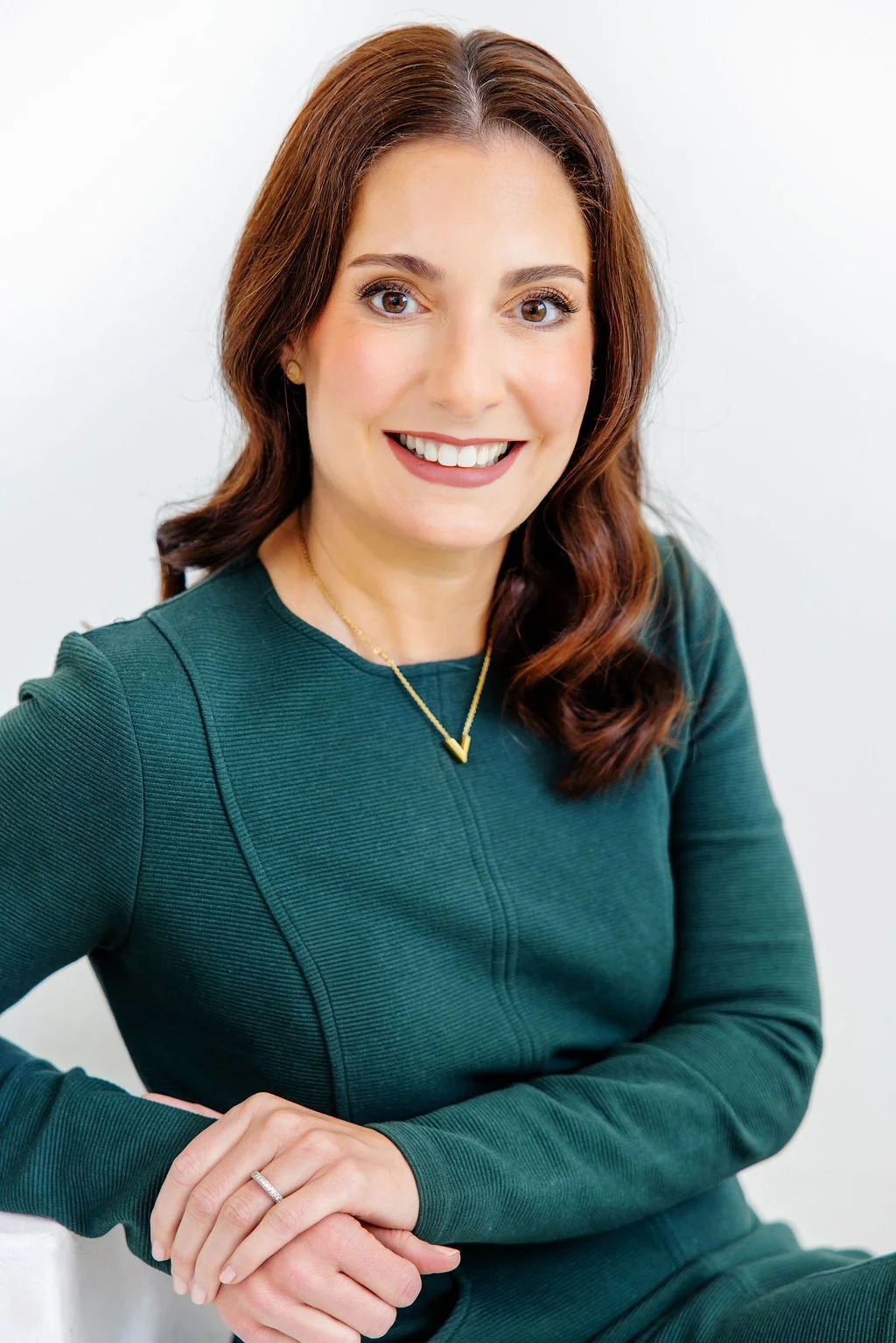 Alison DeVillier, personal injury attorney, smiling, wearing a dark green top, gold necklace, and a ring, sitting against a plain white background.
