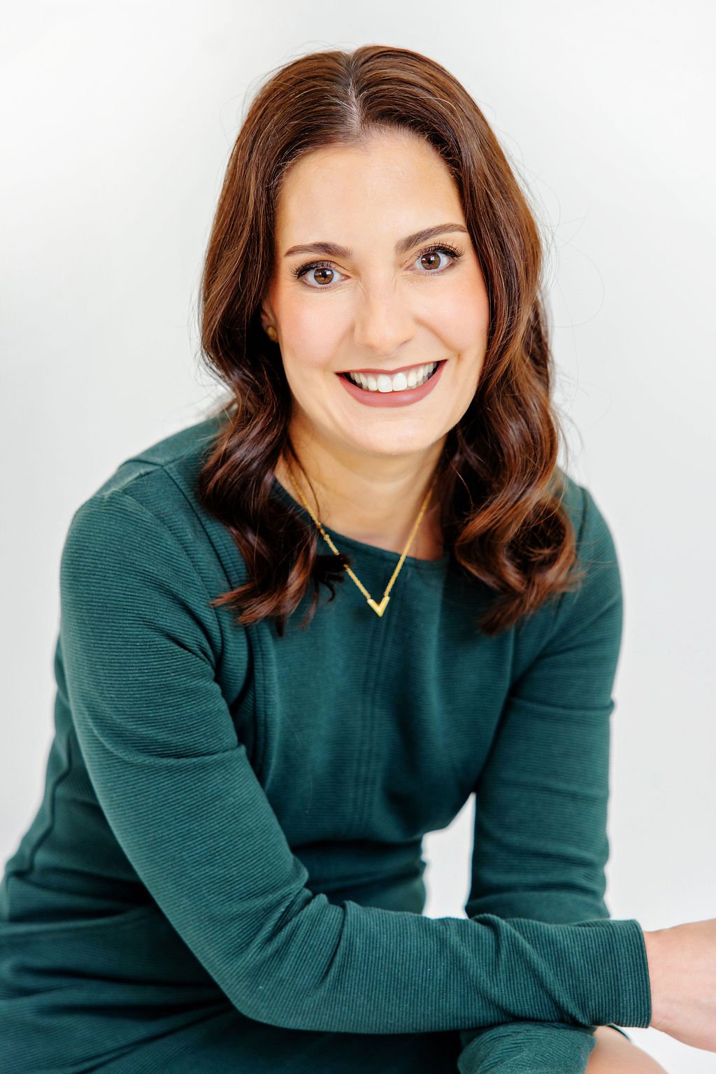 Allison De Villiers headshot smiling, wearing a green top and a gold necklace, sitting against a plain white background.