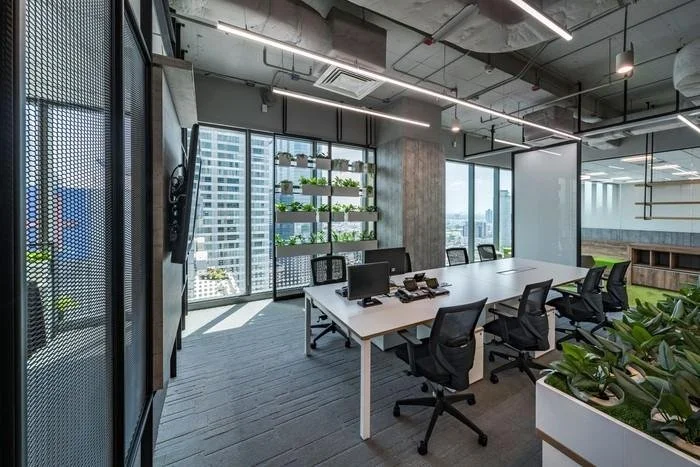 Modern conference room with large windows, office chairs around a white table, and a wall-mounted shelving unit with plants.