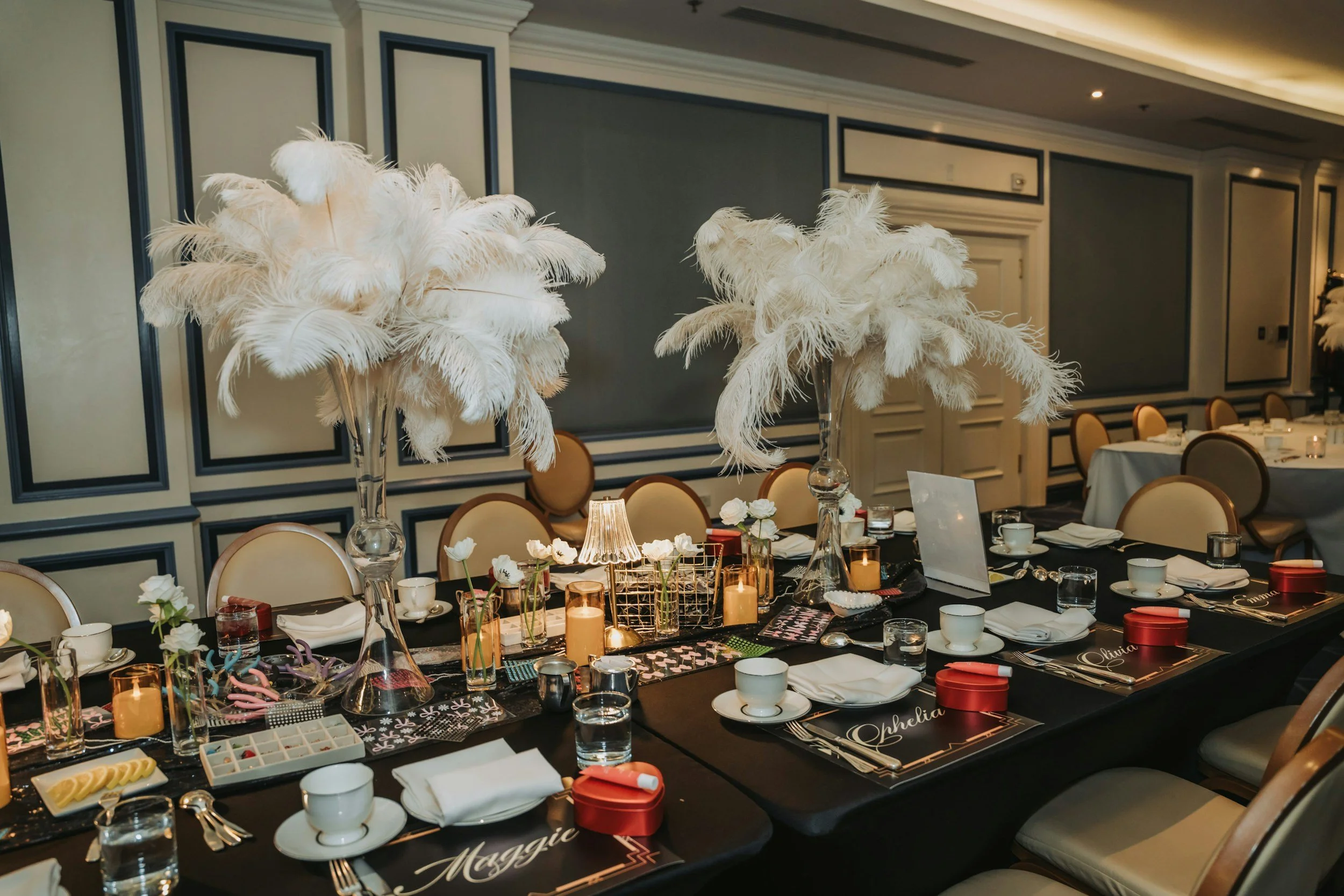 Decorated banquet table with white feather centerpieces, candles, and place settings in a formal dining room.