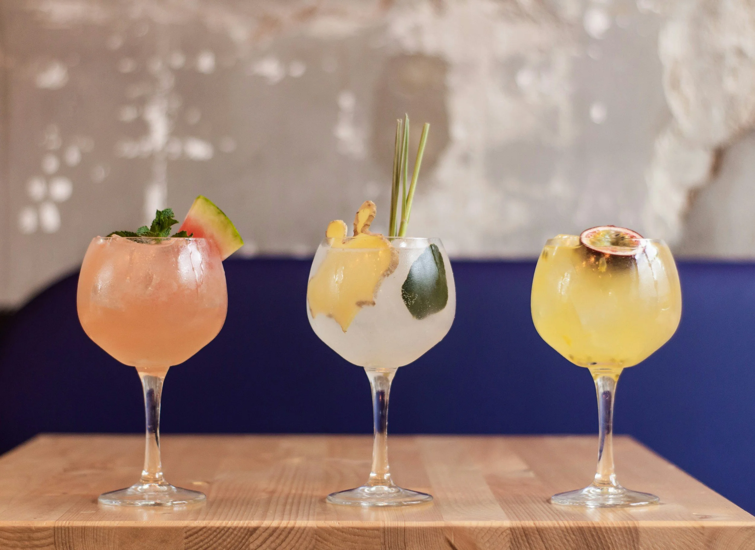 Three colorful cocktails in elegant glasses with fruit garnishes on a wooden surface.