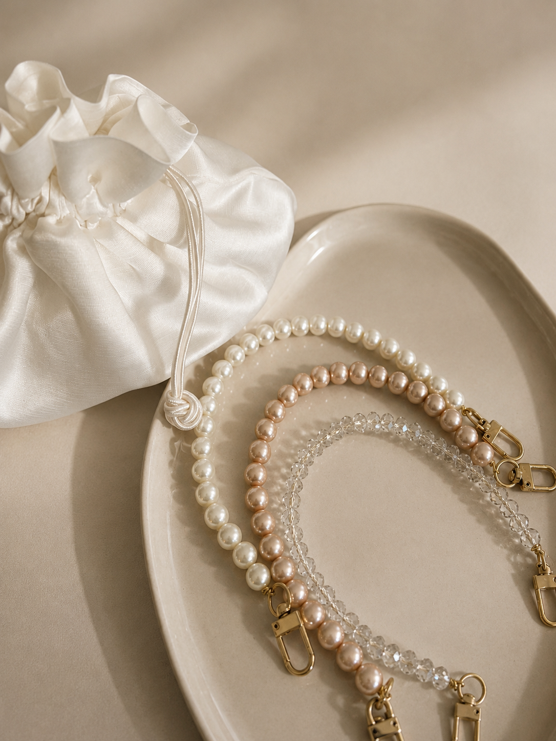 Pearl and crystal beaded bag straps with gold clasps on a beige tray.