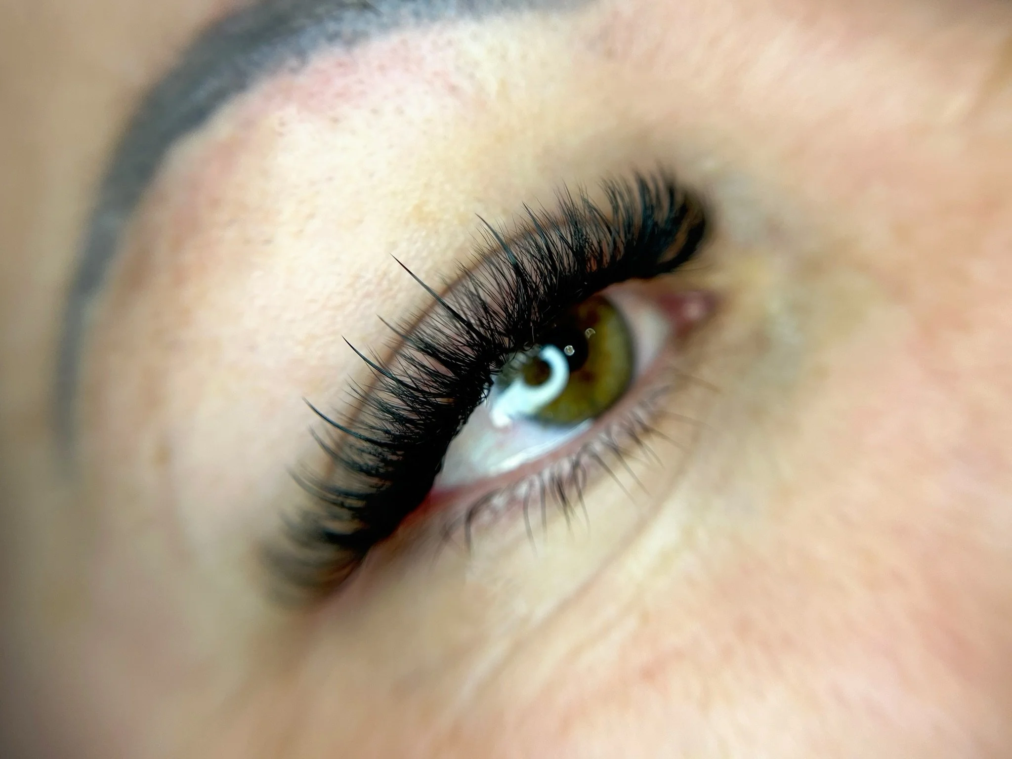 Close-up of a person's eye, showcasing long eyelashes, green iris, and part of eyebrow, with soft skin around the eye.