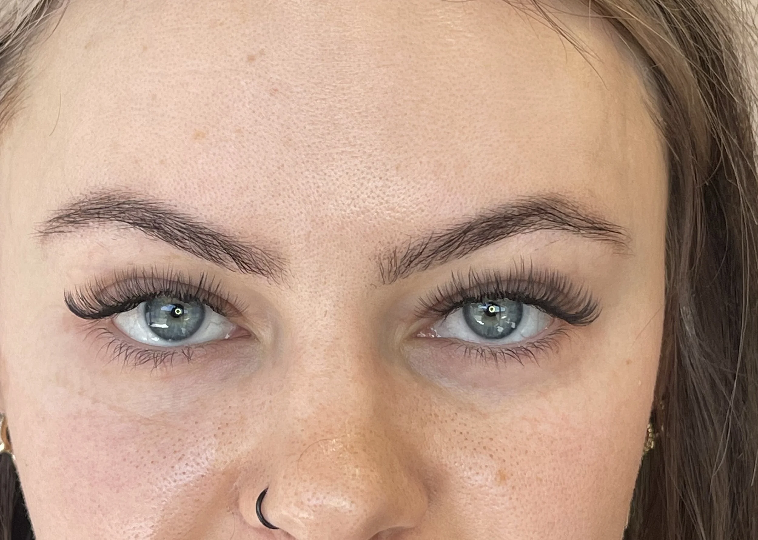 Close-up of a woman's face showing her blue eyes, eyebrows, and forehead with natural skin texture and few small freckles.