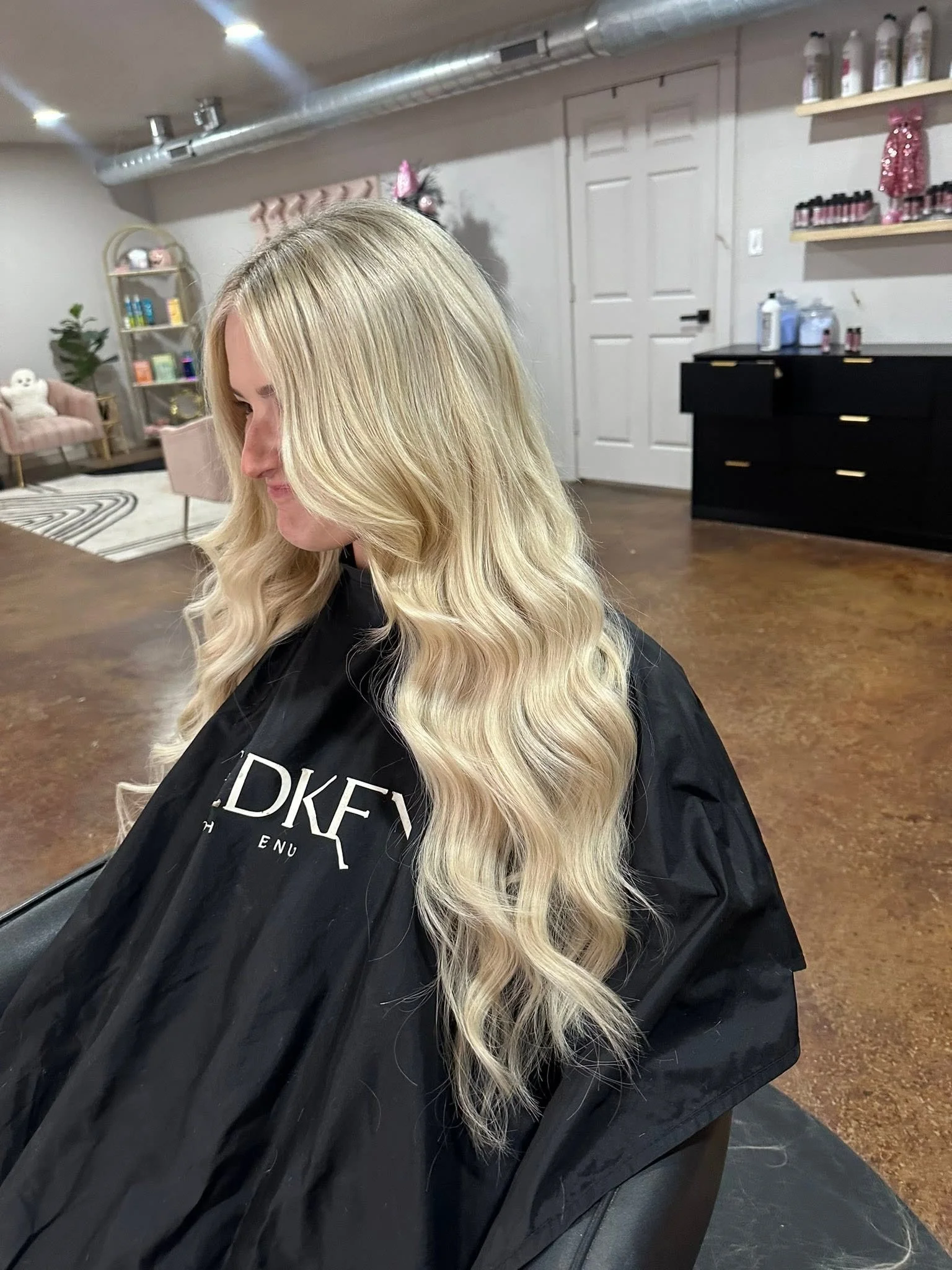 Woman with long blonde hair sitting in a salon chair, getting her hair styled or dyed.