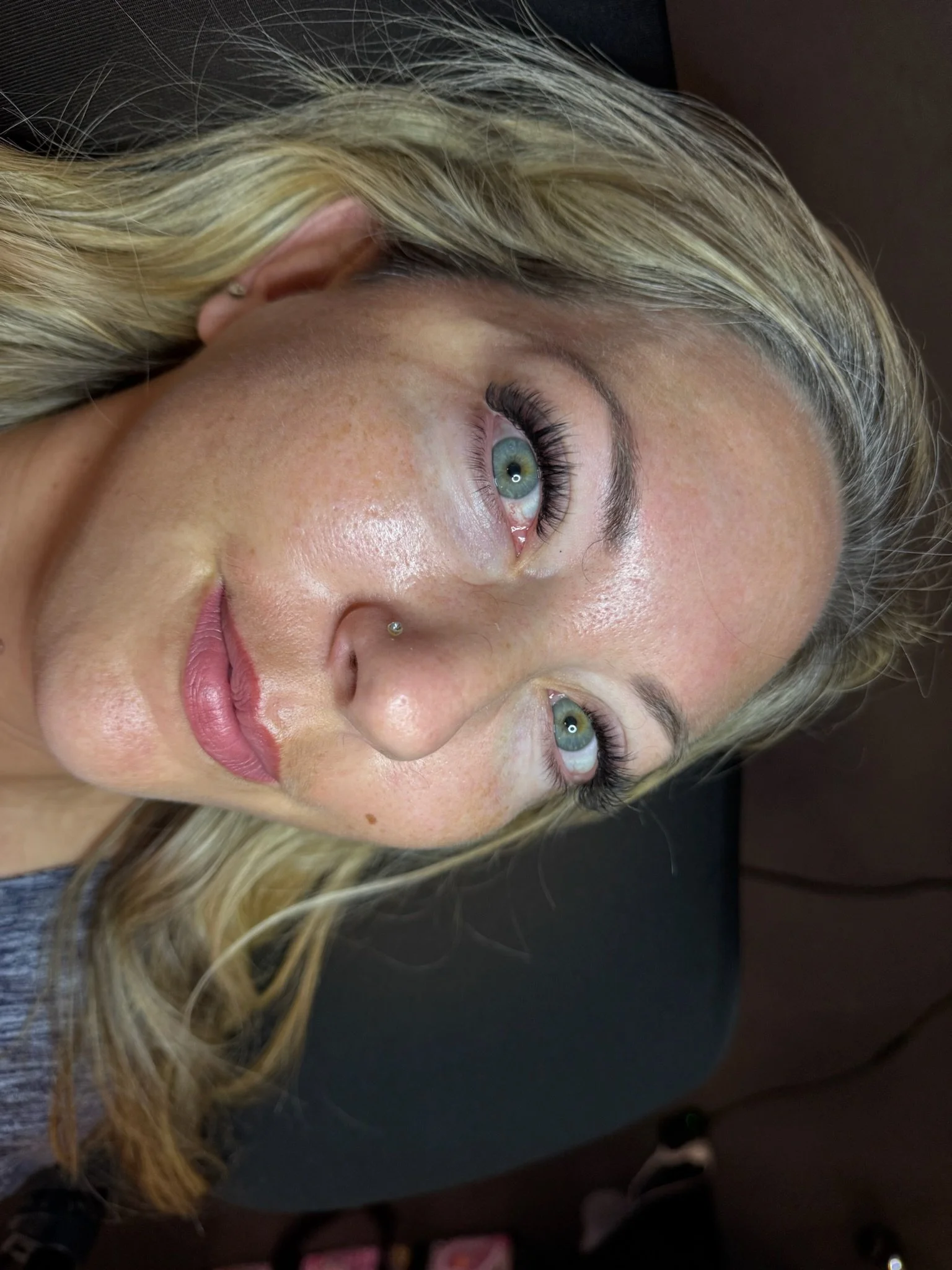 Close-up of a woman with blonde hair, blue eyes, and a nose stud, lying down.
