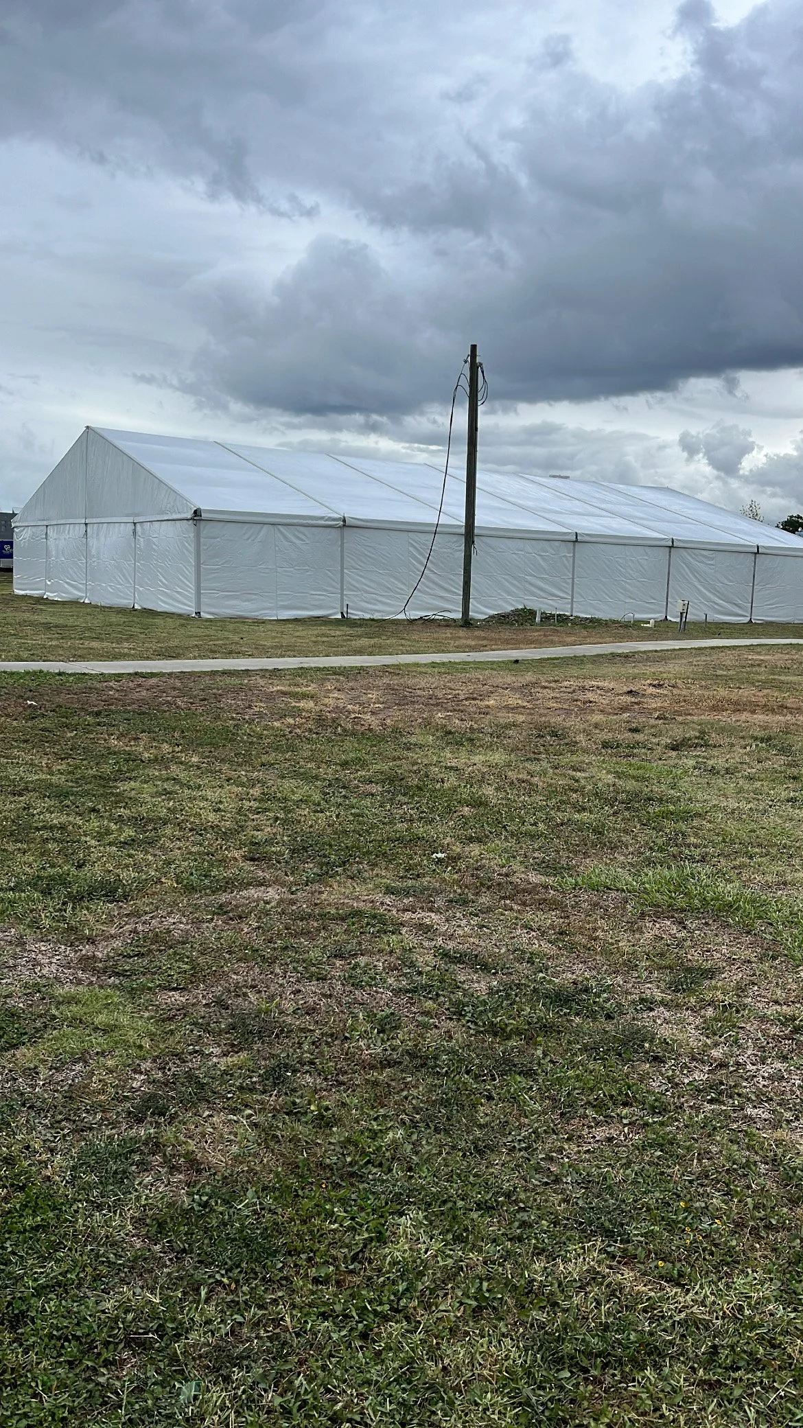 Large white event tent set up outdoors on grassy area with dark cloudy sky overhead.
