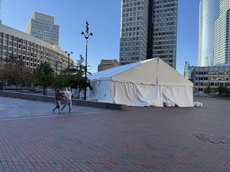 A large white event tent set up in an urban plaza surrounded by tall skyscrapers, with two people walking nearby and some trees along the edge of the plaza for Larkin's Industrial Tents.