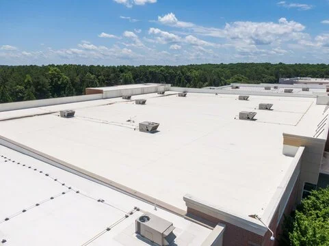 A large commercial building rooftop with multiple ventilation units, under a blue sky with scattered clouds.