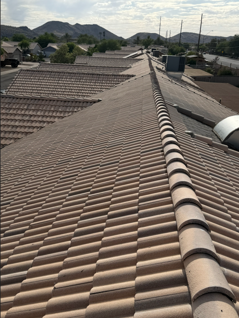 View of a rooftop with tan-colored curved ceramic tiles on a residential building, with other rooftops and mountains in the background.