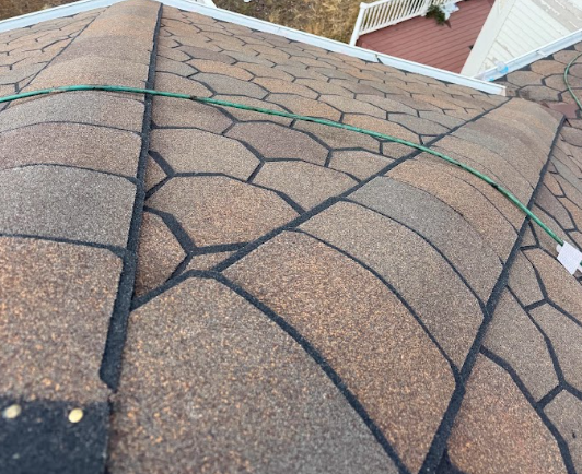 Close-up of a roof with asphalt shingles and a green wire stretched across.