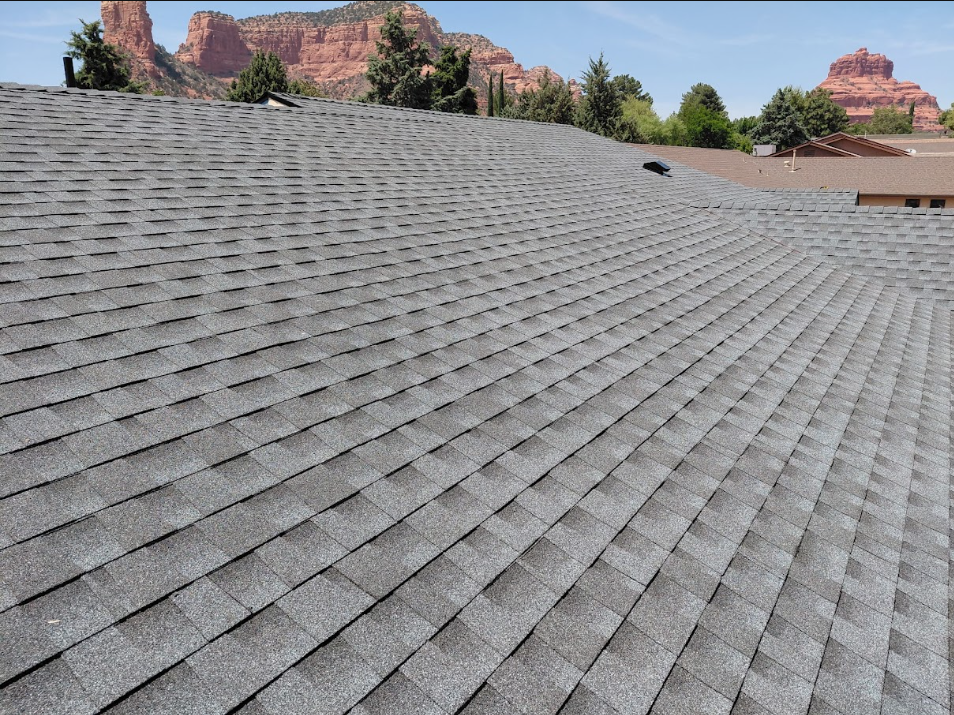 A gray shingled roof with a backdrop of red rock formations and greenery, with a clear blue sky.