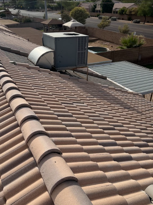 View of a rooftop with an HVAC unit and ductwork, overlooking neighboring rooftops, a street, and some trees in a suburban area.