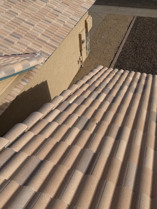 Close-up view of a beige tiled roof and a section of a concrete sidewalk outside a house.