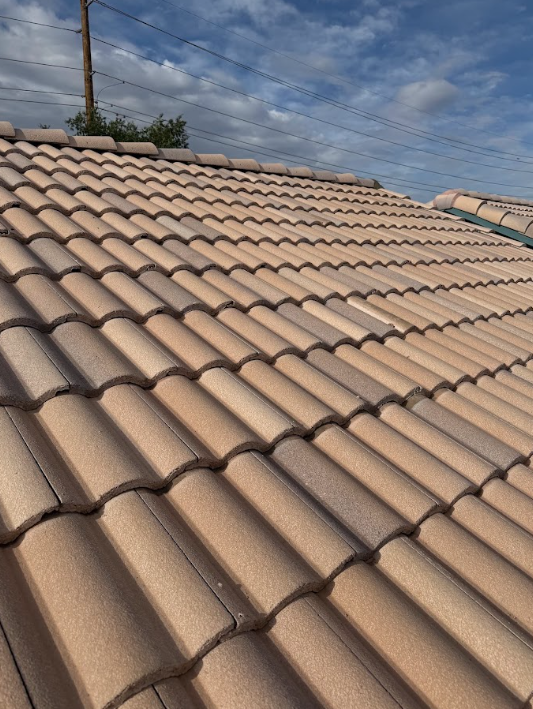 Close-up of a beige tiled roof with weathered tiles, under a partly cloudy sky.