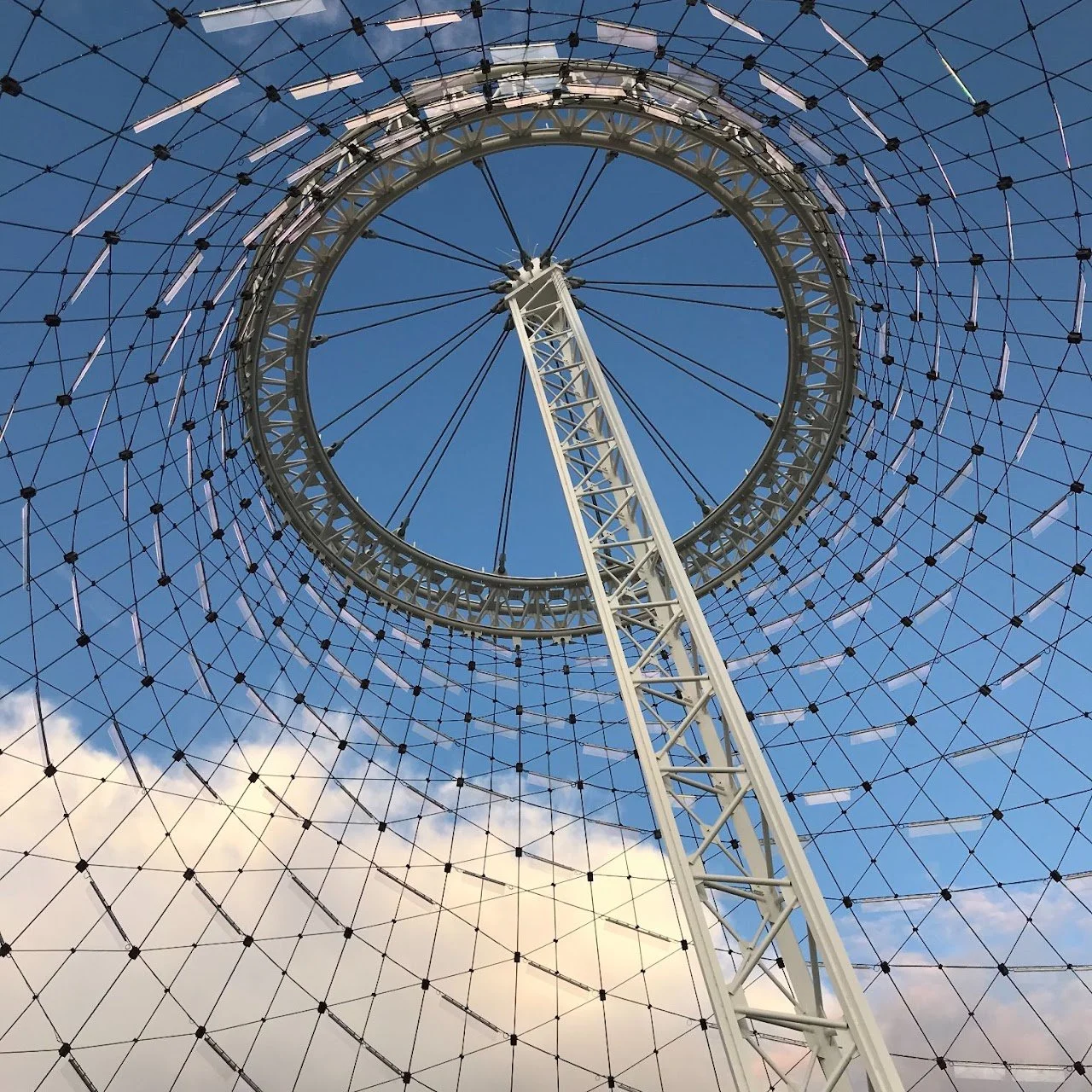 Looking up at a large Ferris wheel against a blue sky with some clouds.