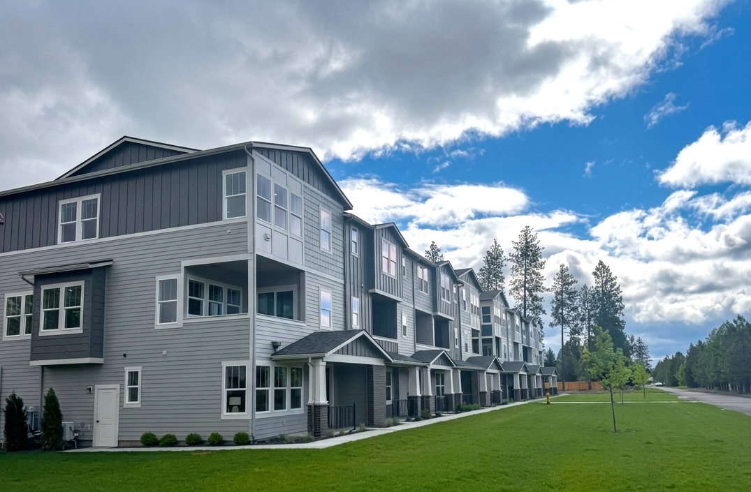 A modern multi-story apartment building with a landscaped lawn in front, under a partly cloudy sky.