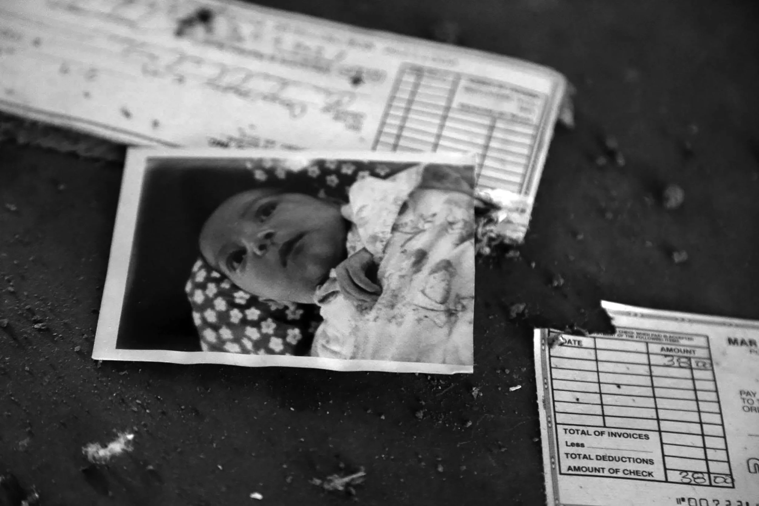 Black and white photo of torn and crumpled photographs and a small invoice on a dark surface.