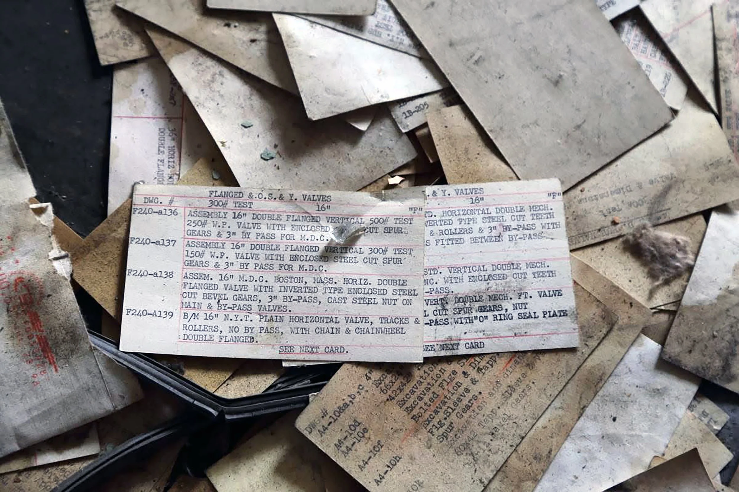 A pile of old, yellowed paper tags with handwritten and printed technical information about valves. The tags include details such as specifications, assembly instructions, and testing notes.
